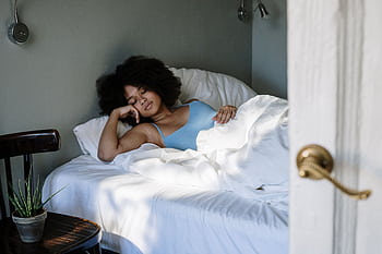 A woman peacefully sleeping in a cozy bedroom with natural light and white linens. HD wallpaper