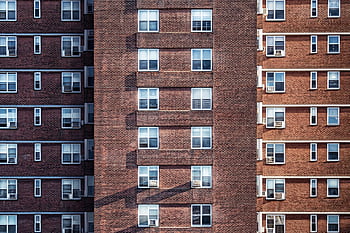 Close-up view of a high-rise brick building facade with multiple windows and air conditioning units. HD wallpaper