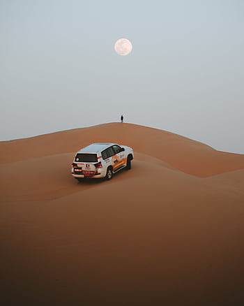 Capture the serene beauty of a desert night under a full moon in Abu Dhabi, featuring endless dunes and a lone car. HD phone wallpaper