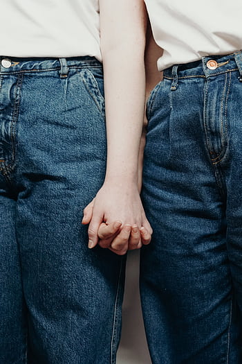 Intimate close-up of a couple in denim jeans holding hands, symbolizing love and connection. HD phone wallpaper