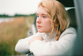 A woman with braided blonde hair gazes thoughtfully from a car window, capturing a serene moment. HD wallpaper
