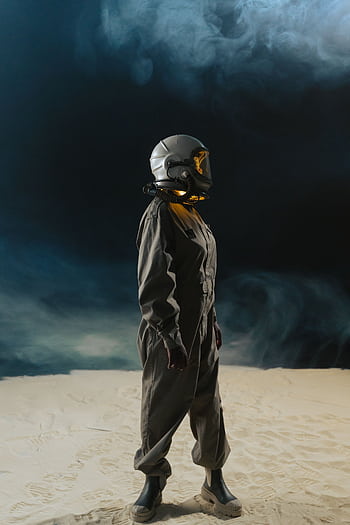 Astronaut in space suit with helmet stands in foggy desert, side view against dark backdrop. HD phone wallpaper