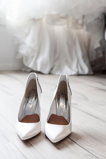 Stylish white bridal shoes positioned in front of a flowing wedding dress indoors. HD phone wallpaper