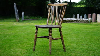A vintage wooden chair sits alone in a serene cemetery surrounded by tombstones. HD wallpaper