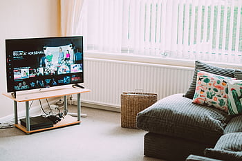 Chic and comfortable living room featuring a modern sofa, decorative pillows, and a TV streaming popular shows. HD wallpaper