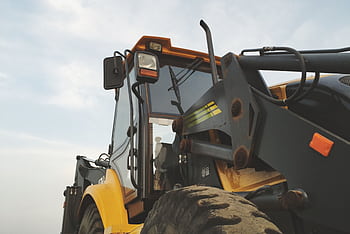Detailed view of a yellow excavator against a clear sky at a construction site. HD wallpaper