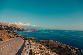 Breathtaking view of a coastal road alongside the ocean with clear blue skies and rugged terrain. HD wallpaper