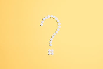 White pills arranged into a question mark shape on a vibrant yellow background. HD wallpaper