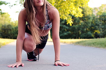 Young woman in athletic wear ready to sprint on a sunny day. HD wallpaper