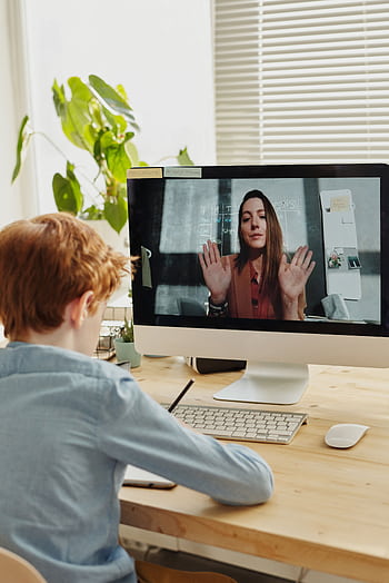 A child participates in online learning through a video call with a teacher, using a setup indoors. HD phone wallpaper
