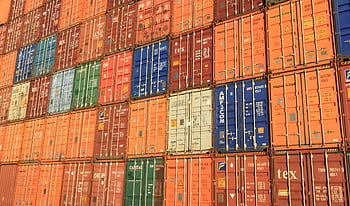 Colorful shipping containers stacked in a harbor, symbolizing global trade. HD wallpaper