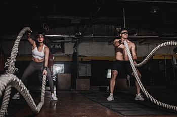 Two people engage in a powerful indoor battle rope workout, showcasing strength and energy. HD wallpaper