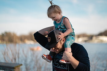Father carrying daughter on shoulders by the lake, sharing a joyful moment together. HD wallpaper