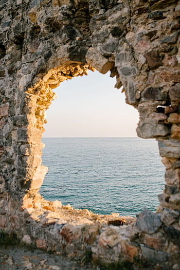 View of the serene ocean through a stone wall's natural opening at sunset. HD phone wallpaper