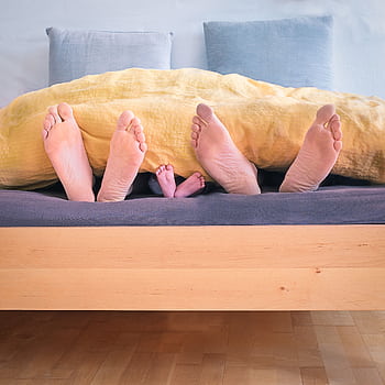 Cozy family moment with baby and parents' feet under a warm blanket in bed. HD phone wallpaper