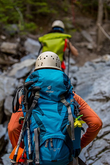 Two hikers with backpacks and helmets navigating a rocky trail in the forest. HD phone wallpaper