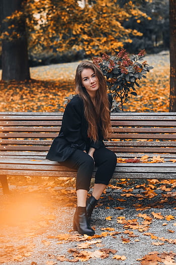Stylish woman with long hair posing on a bench surrounded by autumn leaves. HD phone wallpaper