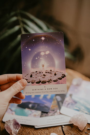 Tarot card held in hand, surrounded by crystals and plants, indoors. HD phone wallpaper