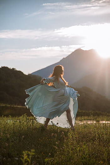 A woman in a flowing blue dress dances gracefully at sunset with mountains in the background. HD phone wallpaper