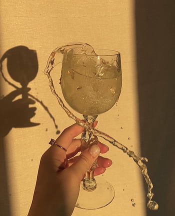 A hand holds a crystal wine glass with liquid splashing in warm sunlight. HD phone wallpaper