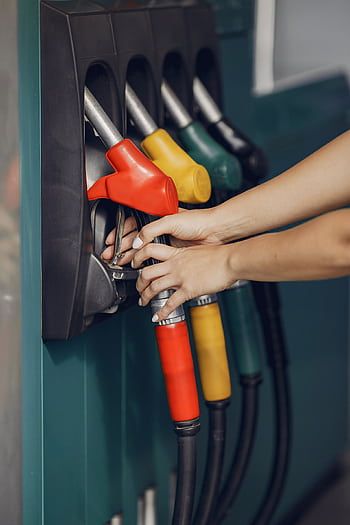 Woman's hands refueling vehicle at gas station with colorful fuel nozzles. HD phone wallpaper