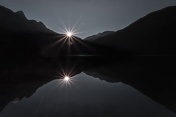 Captivating silhouette of mountains at sunset with sun and reflection over calm lake. HD wallpaper