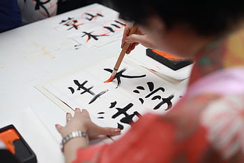 Close-up of a person practicing traditional Japanese calligraphy with a brush on paper. HD wallpaper