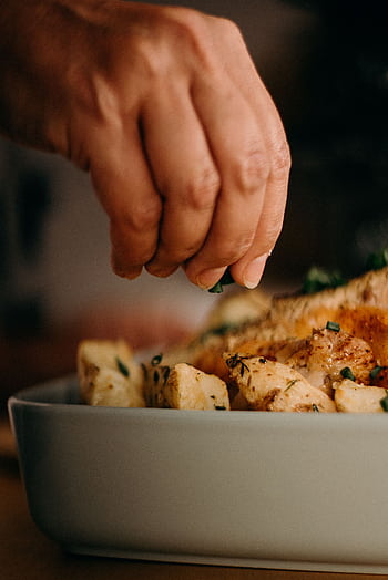 Close-up of a chef's hand garnishing roasted potatoes with herbs, enhancing culinary presentation. HD phone wallpaper