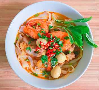 A vibrant bowl of Vietnamese noodle soup with shrimp, herbs, and quail eggs. HD wallpaper