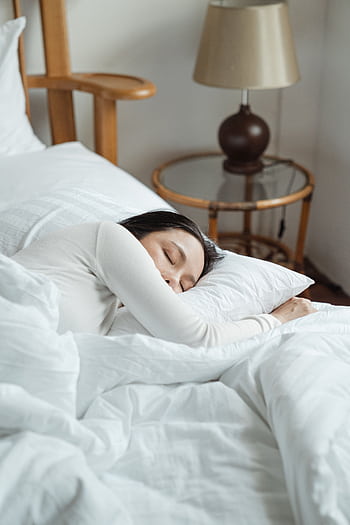 A serene scene of a woman sleeping peacefully on white bedding in a cozy bedroom. HD phone wallpaper