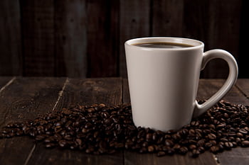 A rustic ceramic mug filled with hot coffee, surrounded by coffee beans on a wooden table. HD wallpaper
