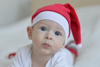 A cute baby with blue eyes wearing a red Santa hat, capturing the festive Christmas spirit indoors. HD wallpaper