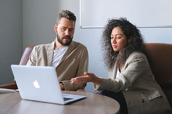 Two business professionals in an office having a discussion over a laptop. HD wallpaper