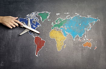 A hand guides a toy airplane over a colorful world map drawn on a chalkboard, symbolizing travel and exploration. HD wallpaper