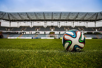 Close-up of a soccer ball on a lush grass field with an empty stadium in the background. HD wallpaper
