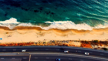 Stunning aerial view of a highway parallel to a tranquil beach and ocean waves. HD wallpaper