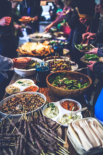 A vibrant buffet spread with salads, skewers, and dips at a lively indoor gathering. HD phone wallpaper