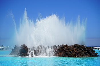 Capturing a powerful wave splash against rocks on a clear blue beach day. HD wallpaper