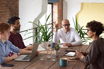 A group of colleagues in a modern office having a strategic discussion around a wooden table. HD wallpaper