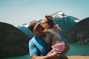 Tender moment of a father and daughter hugging in a scenic mountain setting. HD wallpaper