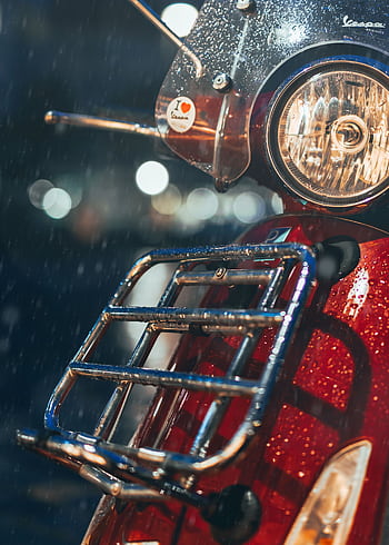 Close-up of a classic red scooter in the rain, capturing a bokeh background, evoking a vintage travel vibe. HD phone wallpaper