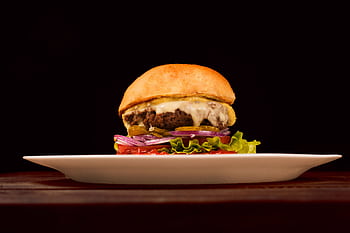 Mouth-watering cheeseburger with fresh veggies and melted cheese on a white plate. HD wallpaper