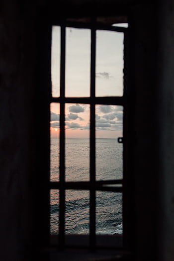 Dramatic ocean view with a sunset framed through window bars, evoking a sense of dom. HD phone wallpaper