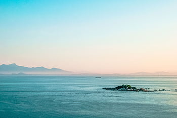 A tranquil seascape with a distant island and mountains under a soft morning sky. HD wallpaper