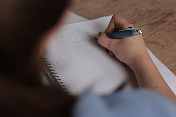 A student writes mathematical notes in a notebook using a pen, focus on studying. HD wallpaper