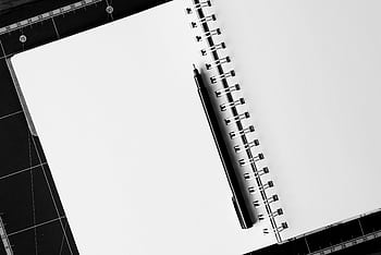 Top view of an open spiral notebook with a black pen on a cutting mat, perfect for creative projects. HD wallpaper