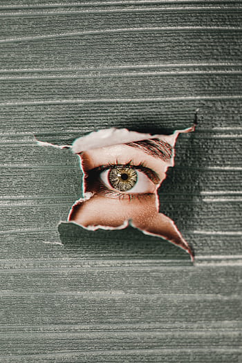 Close-up of an eye peering through a torn paper hole, creating a sense of mystery. HD phone wallpaper