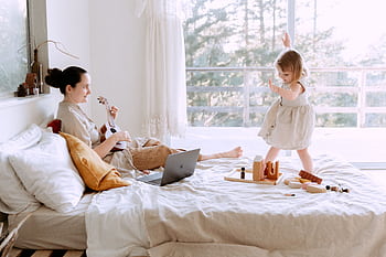 A joyful mother plays ukulele while her daughter dances in a sunlit bedroom. HD wallpaper