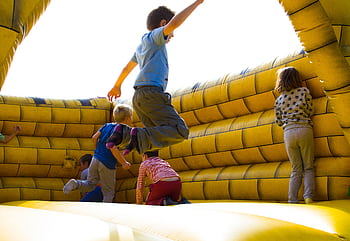 Kids enjoying a fun time bouncing in a vibrant inflatable castle outdoors. HD wallpaper