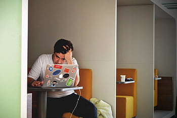 Man showing stress and frustration while working remotely on a laptop indoors. HD wallpaper